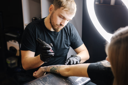 Tatoeëerder zet een tattoo op de arm van een cliënt. 

